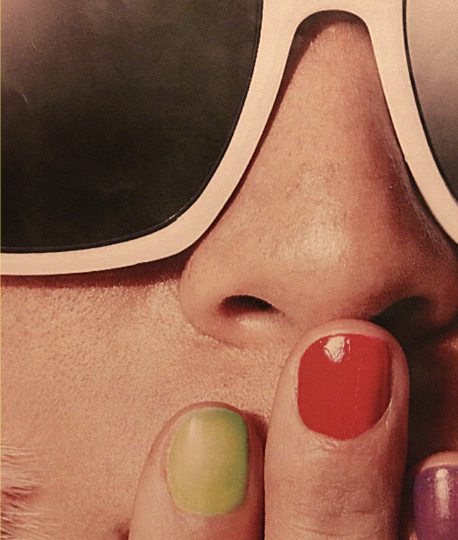 Close-up of someone in white sunglasses holding a finger to their lips